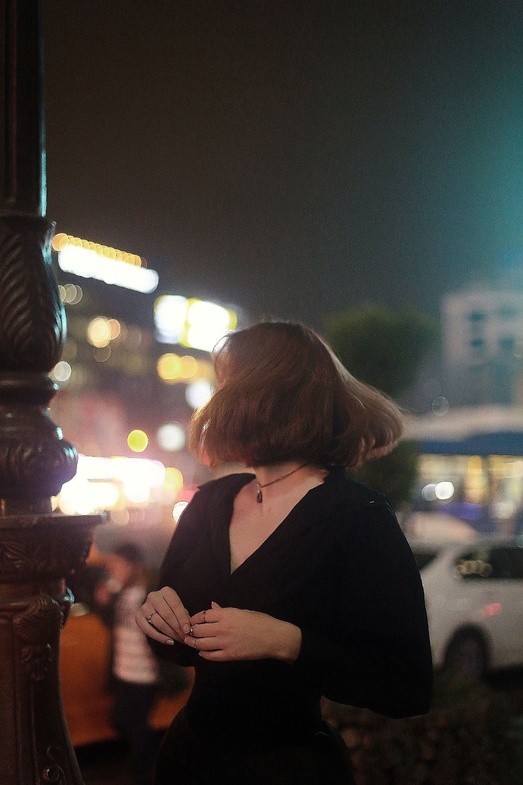夜の街の灯りの中に立つ、黒いドレスの女性（イメージ）